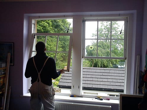 A man in overalls stands by a window, focused on installing sash windows with precision and care.